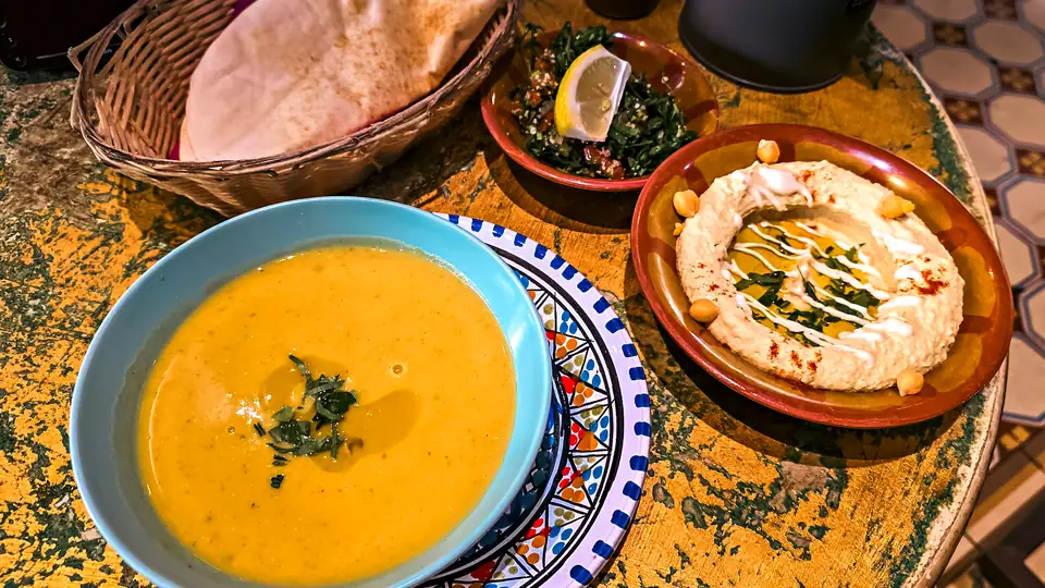 Lentil soup, hummus with chickpeas, tabbouleh and flatbread on a painted table