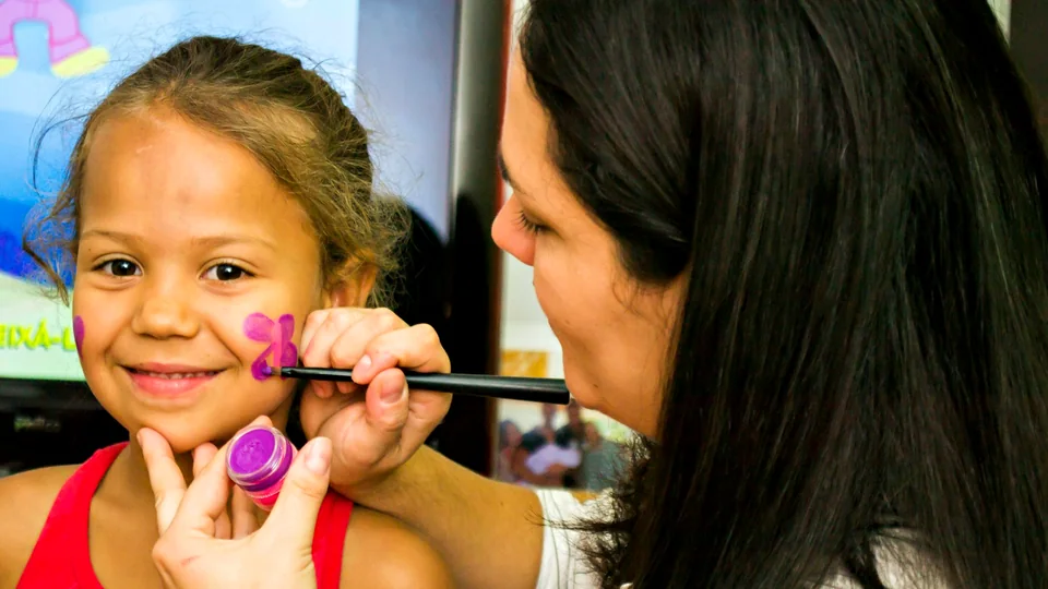 A smiling girl has a purple butterfly painted on her cheek
